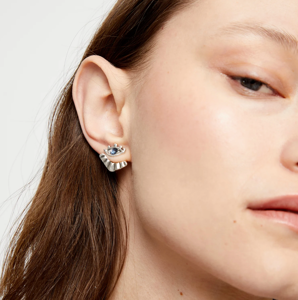 Pendientes bañados en plata en forma de ojo con pestañas y cristal facetado azul